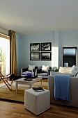 Various seating, pale pouffe and armchairs in background below collection of pictures on living-room wall painted pale blue