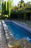 Lang gestreckter Pool mit verwitterter Steineinfassung in mediterranem Garten