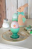 Boiled egg in turquoise eggcup in front of textile rabbit-shaped egg warmers