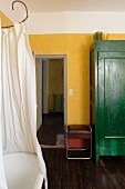 Nostalgische Badewanne mit weißem Duschvorhang und grün lackierter Schrank an gelber Wand