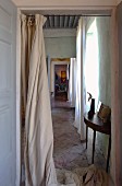 View of delicate console table on vintage stone floor through open doorway with floor-length curtain