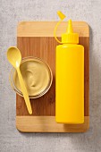 Mustard in a glass bowl next to a yellow plastic bottle