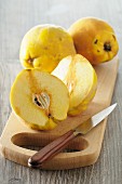 Quinces, whole and halved, on a chopping board with a knife