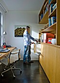Mann in schmalem Arbeitszimmer mit Klassiker Bürostuhl vor Schreibtisch und Einbauschrank aus Holz