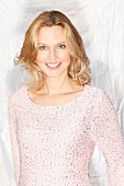 A blonde woman wearing a pastel pink jumper with Lurex and sequins