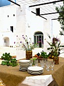Ochre tablecloth, crockery and vases of Mediterranean flowers on table under pergola outdoors