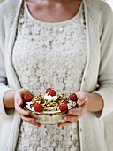 A woman holding a bowl of white chocolate mousse with honey, roasted nuts and fresh raspberries