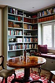 Round table and antique-style chairs in front of fitted bookcases and custom window seat