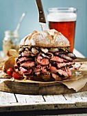 A giant steak sandwich on a wooden board with a beer