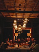 Gäste um Tisch unter beleuchteten Draht-Pendelleuchten in gemütlicher Stimmung in Safari-Lodge