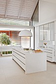Free-standing white counter below hemispherical pendant lamp in open-plan designer kitchen
