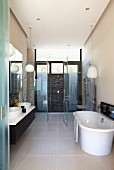 Modernes Bad mit freistehender Badewanne auf grossformatigem Fliesenboden vor verglastem Duschbereich