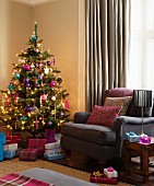 Decorated Christmas tree and presents next to brown armchair in corner of living room