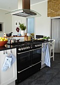Island counter with black gas cooker and extractor hood in renovated kitchen with traditional ambiance