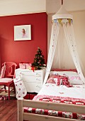 Romantisch dekoriertes Bett mit Baldachin und Patchworkdecke in Mädchenzimmer mit roter Wand