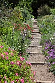 Narrow gravel path with wooden sleepers between bed of flowering plants