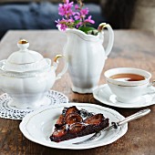 A slice of chocolate cake with plums and icing sugar served with tea