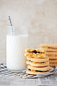A stack of jam and cream biscuits with a glass of milk