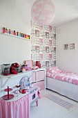 Mädchenzimmer mit rosa Farbakzenten, Kinderküche, Bett vor tapezierter Wand mit Häusermotiv