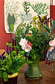 Blumenstrauss in grüner Vase auf Tisch, im Hintergrund Bild mit nostalgisch gezeichneten Pflanzenabbildungen