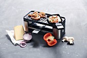 A raclette for two pans with a grill surface surrounded by ingredients for raclette