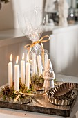 weiße, brennende Kerzen und Moos in Backförmchen, neben Nikolausfigur und Backformen-Set