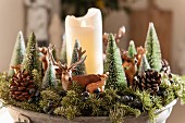 Weihnachtsdeko aus Tannenbäumchen und Tierfiguren um weiße Stumpenkerze dekoriert