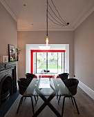 Hängeleuchte mit Glühbirnen über Glastisch mit schwarzen Schalenstühlen in modernisiertem Wohnraum, im Hintergrund breiter Durchgang und Blick auf rote Stahlkonstruktion