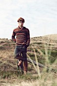 A young red-haired man wearing jeans and a stripy, knitted jumper