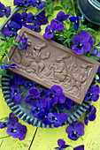 Eine Tafel Schokolade mit Ostermotiv, umgeben von Hornveilchen