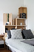 Bed with stacked shelving elements as headboard