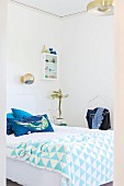 Blick ins Schlafzimmer auf Doppelbett mit weiss-blau gemusterter Tagesdecke und Kissen, oberhalb kugelförmige Wandleuchte