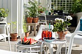 Wassermelone, Erfrischungsgetränke und Geranientopf auf mehrteiligem weißem Beistelltisch-Set auf der Terrasse