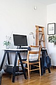 Wooden chair and desk on black wooden trestles in corner of minimalist room