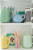 Collection of teapots and coffee pots and colourful drinking straws on white shelves