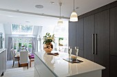 Glossy white island counter and dark brown fitted cupboards in elegant, open-plan kitchen