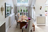 Elegant set dining table with pale upholstered chairs in niche with skylight