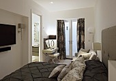Elegantes Doppelbett mit dunkelbrauner Tagesdecke und drapierten Kissen, Schminktisch vor Fenstertür