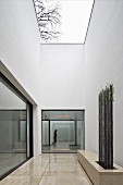 Atriumhaus mit minimalistisch gestaltetem Patio, Steinbank mit Rankstäben und trübem Himmel