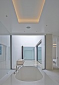 Designer bathtub below ceiling panel with indirect lighting in modern house with atrium