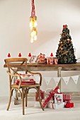 Hängeleuchten über weihnachtlich dekoriertem, rustikalem Holztisch mit Vintagestuhl und Weihnachtsgeschenken in rot-weisser Verpackung