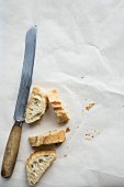 Four slices of baguette on a piece of white paper with a bread knife