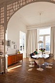 View of elegant dining area with classic designer furniture and mother and child seating around table seen through traditional arched doorway with lead glazing