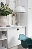 Bouquet and white table lamp on white sideboard behind turquoise classic shell chair