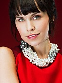Dark-haired woman wearing red sleeveless dress and pearl necklace