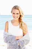 Young blonde woman wearing white top and lilac cardigan on beach