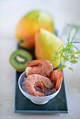 Prawns on ice with a mango, a pear and a kiwi in the background