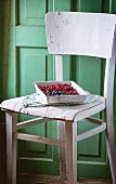 Blackberries and lingonberries on a vintage tray on an old white wooden chair against the green wooden wall