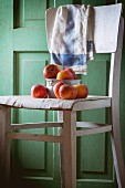 An aluminium bowl of red apples on an old white wooden chair against green wooden wall