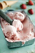 Strawberry yoghurt ice cream in an ice cream container with an ice cream scoop